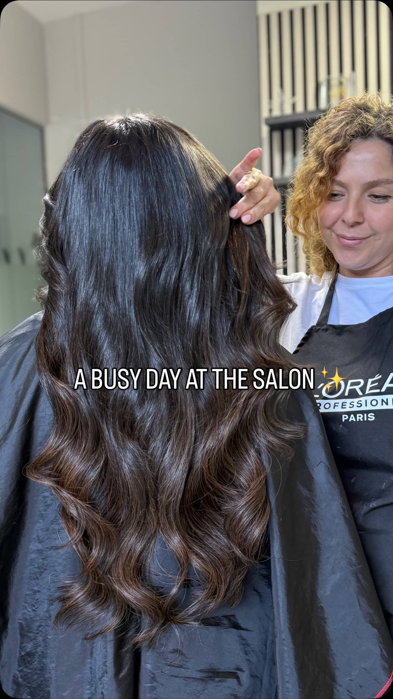 Greta showing a client's long glossy dark brunette waves in the salon